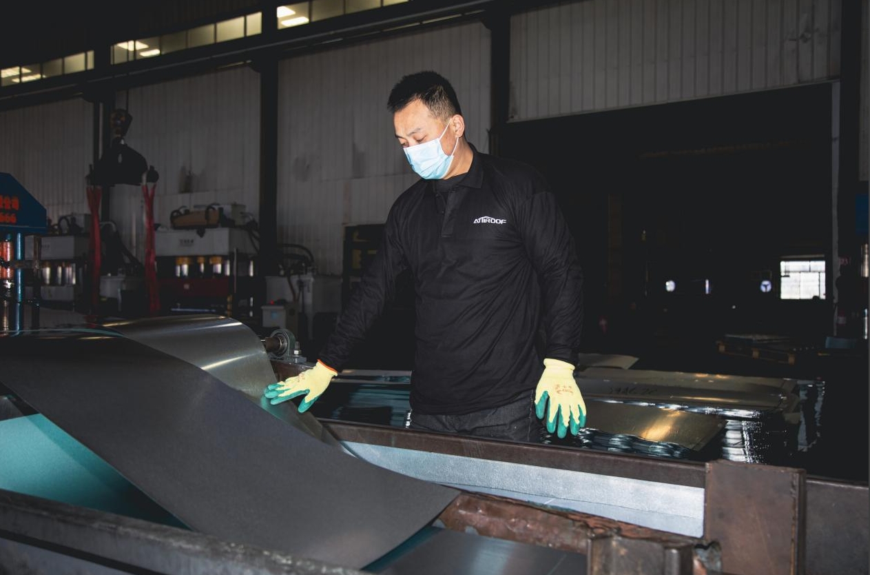 Attiroof's worker inspecting galvanized steel sheets for stone-coated metal roof tile production in a factory.